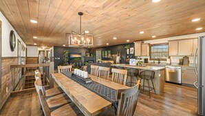 Une cuisine spacieuse avec un plancher en bois, un coin repas avec une longue table et des chaises, et un bar avec des tabourets.