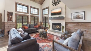 A spacious living room with a fireplace, large windows, and a high ceiling. - Family Retreat - Pool, Game Room, Theatre, Bowling (Sevierville)