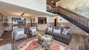 A spacious living area with a large couch, two armchairs, and a coffee table. A staircase with a wooden railing leads to an upper level. - Family Retreat - Pool, Game Room, Theatre, Bowling (Sevierville)