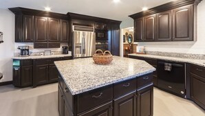 A modern kitchen with dark cabinetry, granite countertops, stainless steel appliances, and a central island with a basket. - Family Retreat - Pool, Game Room, Theatre, Bowling (Sevierville)