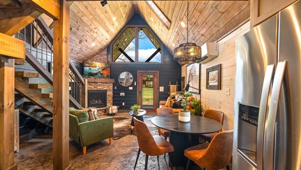 A cozy interior with a stone fireplace, wooden ceiling, and a dining area with a round table and chairs. - Cozy Honeymoon Cabin w/ Mtn Views-Hot Tub-Fire Pit (Sevierville)
