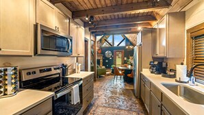 A kitchen with a large stove, microwave, and stainless steel sink. There is a dining area with a table and chairs visible through an open doorway. - Cozy Honeymoon Cabin w/ Mtn Views-Hot Tub-Fire Pit (Sevierville)