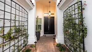 A narrow pathway leading to a dark door, flanked by white walls and a black metal fence with climbing plants. - 4br, 3ba, pool near TPC in Scottsdale (Scottsdale)