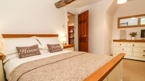 A bedroom with a wooden bed frame, a large mirror, and a dresser with drawers. - Pine Cottage (Appleby-in-Westmorland)