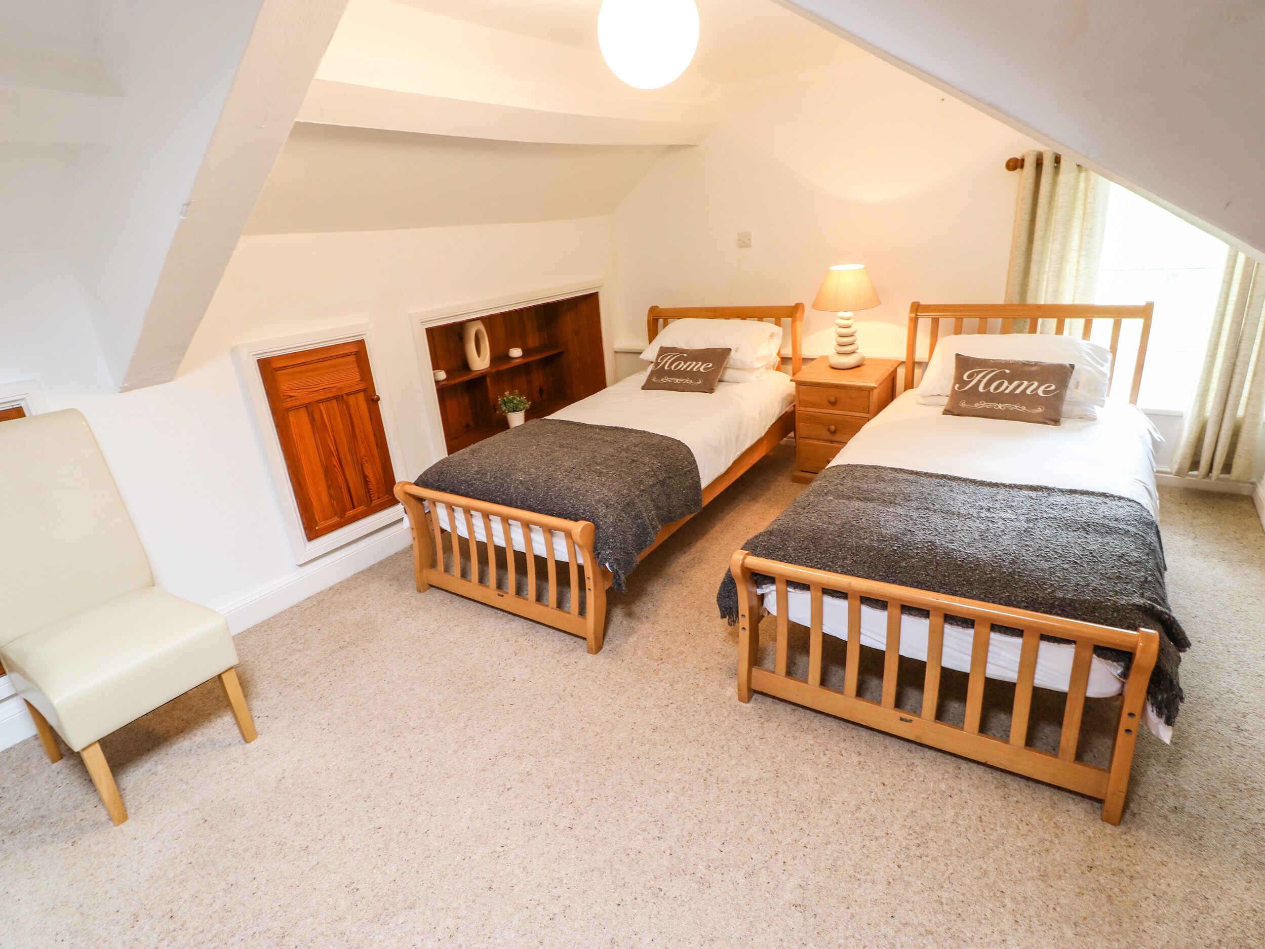 Une chambre à coucher avec deux lits en bois, une petite chaise, une armoire en bois et un luminaire au plafond.