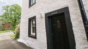 A two-story building with a textured exterior, a black-framed door labeled "Pine Cottage," and a small window. - Pine Cottage (Appleby-in-Westmorland)