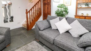 A living room with a grey sofa, a wooden staircase, a mirror, and a plant. - Pine Cottage (Appleby-in-Westmorland)