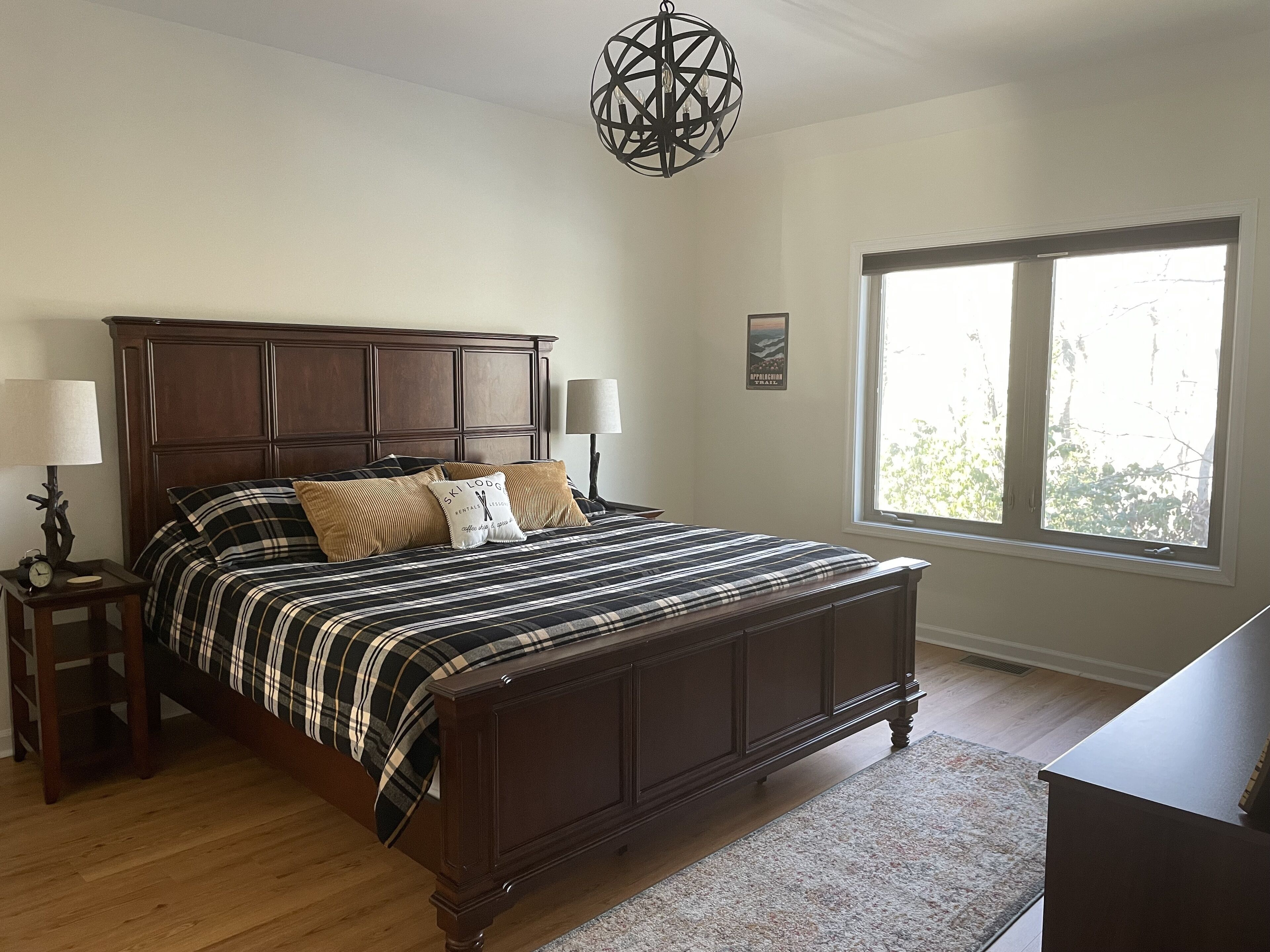 Une chambre à coucher avec un grand lit, deux lampes de chevet, une tête de lit en bois, une fenêtre avec vue et un lustre.