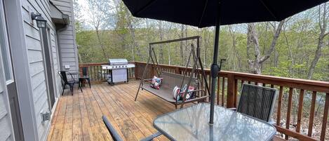 A wooden deck with a glass table and chairs, a swing, and a grill.