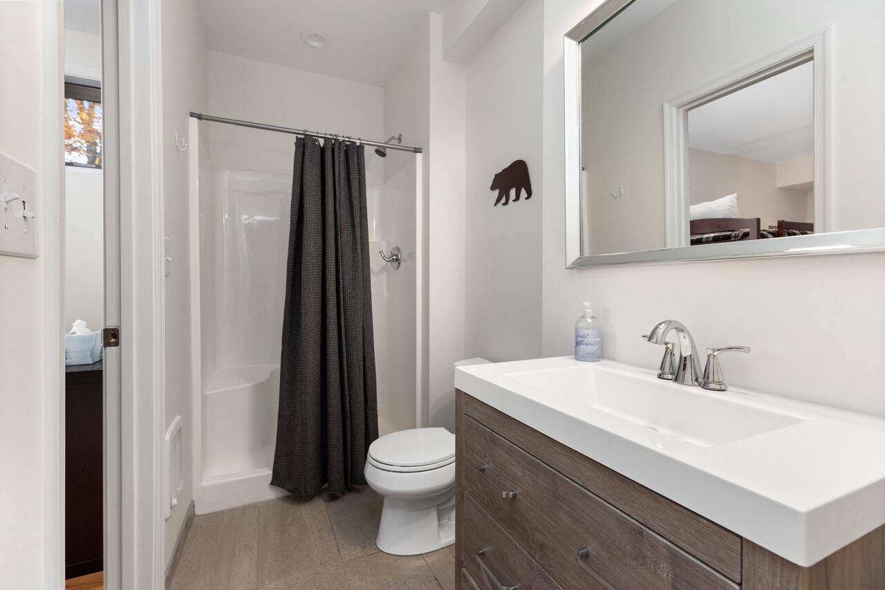 Uma casa de banho moderna com uma sanita, um lavatório branco, um espelho e uma cabine de duche com porta de vidro.