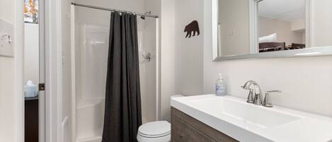 Uma casa de banho moderna com uma sanita, um lavatório branco, um espelho e uma cabine de duche com porta de vidro.
