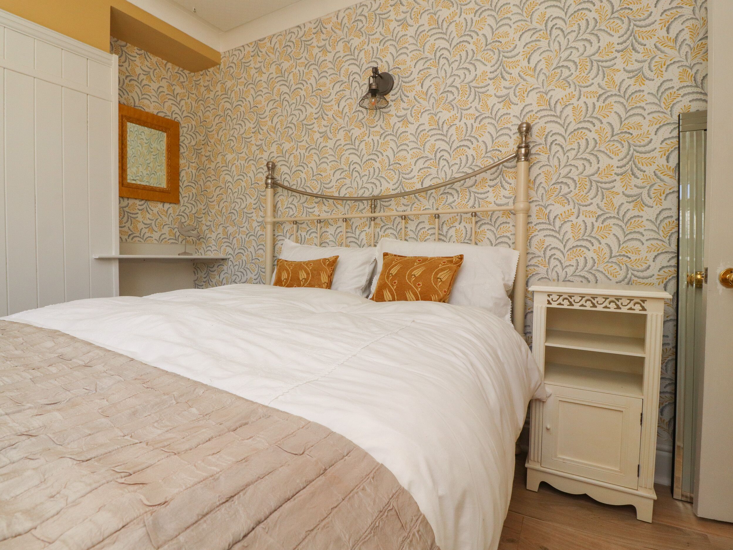 A bedroom with a bed, a nightstand, a wall-mounted lamp, and a door.