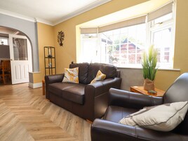 A living room with a brown leather sofa, a wooden herringbone floor, a window with a view of a brick building, and a small side table with a plant.