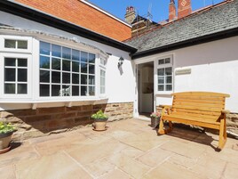 A small, white building with a stone foundation, a wooden bench, and potted plants.