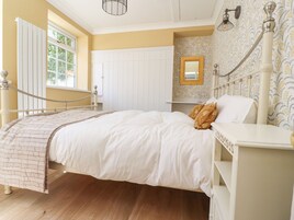A bedroom with a bed, a nightstand, a dresser, a mirror, a window with shutters, and a radiator.