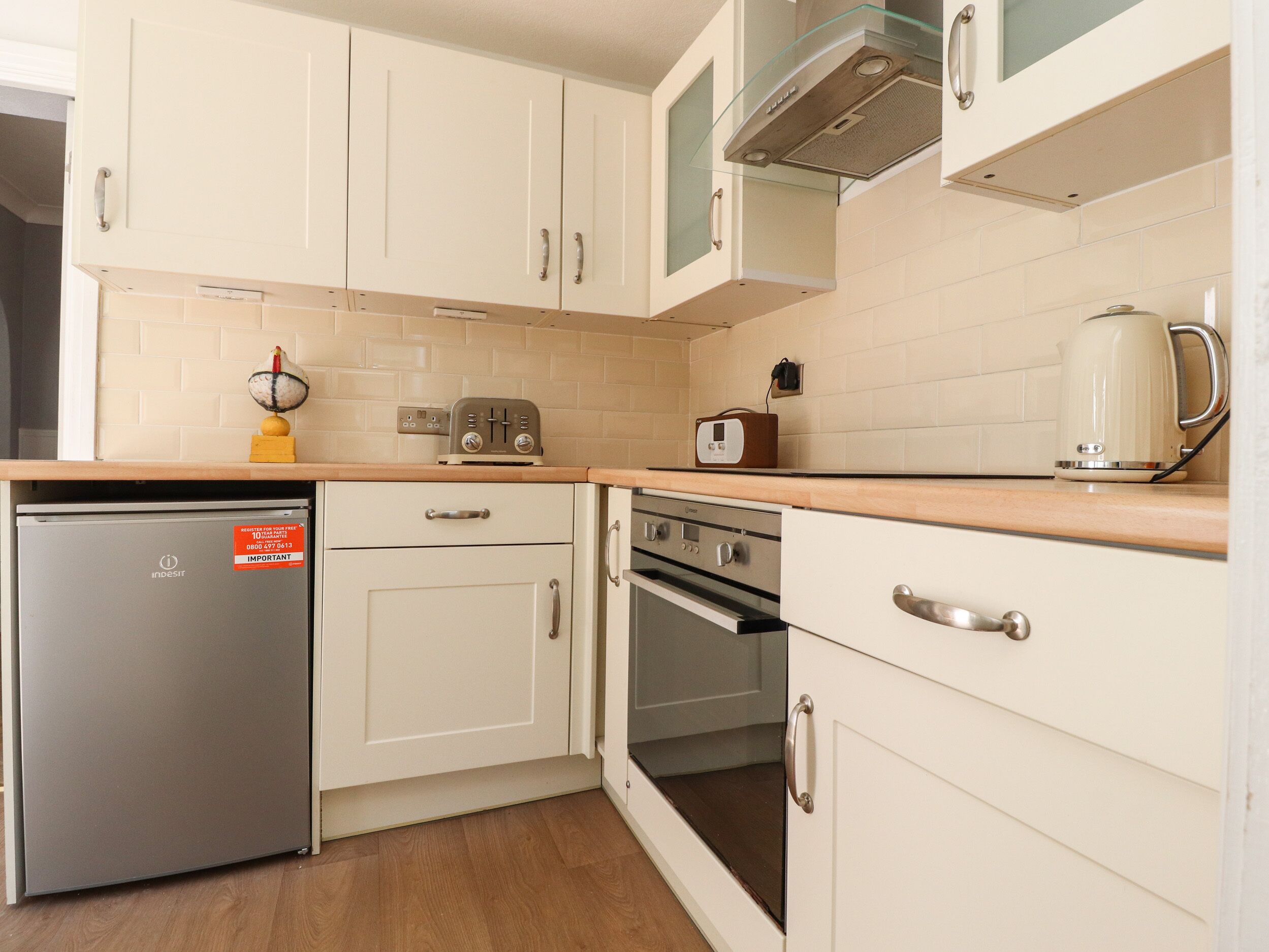 A compact kitchen with white cabinets, a built-in oven, a small refrigerator, and a coffee maker.