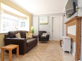A living room with a brown leather sofa, a wooden coffee table, a black armchair, and a white radiator. There is a television mounted on the wall and a small white cabinet.