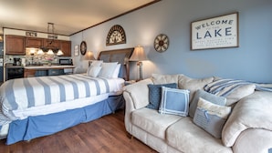 A bedroom with a bed, a couch, a desk, and a kitchen area. - Waterfront studio w/private balcony & stunning views - Marina Cay Vista Aqua Studio (Bigfork)