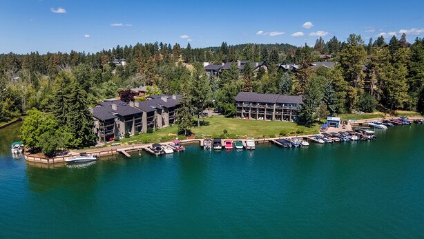 A lakeside hotel with multiple buildings, a dock with boats, and a forested hillside in the background. - Waterfront studio w/private balcony & stunning views - Marina Cay Vista Aqua Studio (Bigfork)