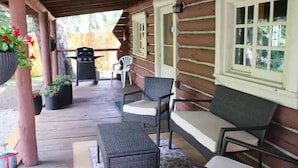 A log cabin with a porch, wicker furniture, a grill, and potted plants.