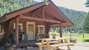 Een rustieke blokhut met een veranda, houten picknicktafel en een barbecueplaats.
