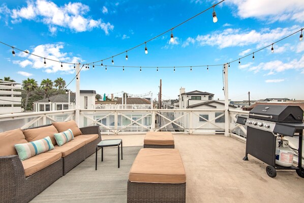 A rooftop patio with a grill, outdoor furniture, and string lights.