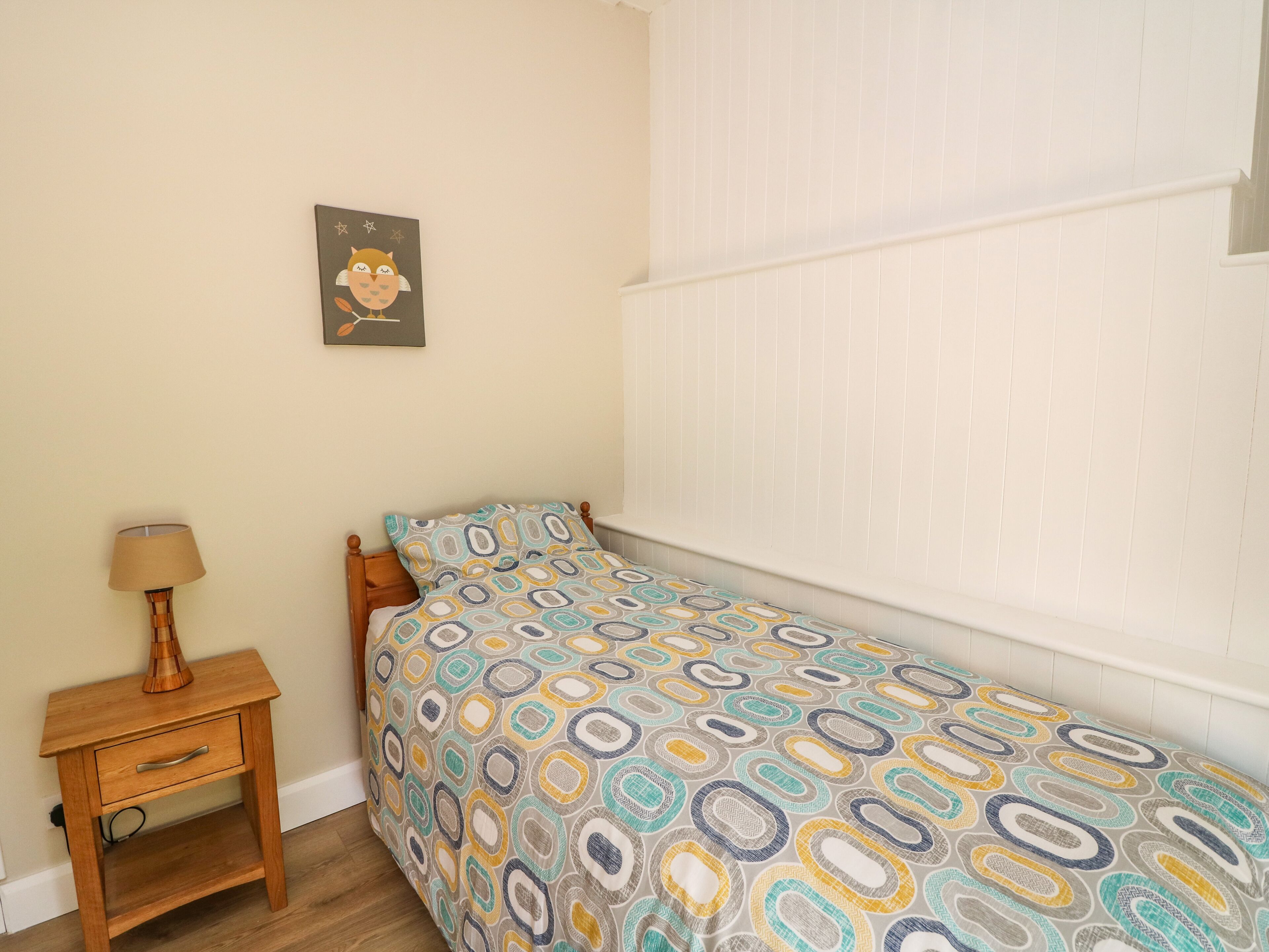 A small bedroom with a bed, a nightstand, a lamp, and a wall-mounted picture.