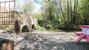 A rustic stone bridge over a stream, surrounded by dense greenery and a picnic table with a sign. - Yew Tree House (Ballindaggan)