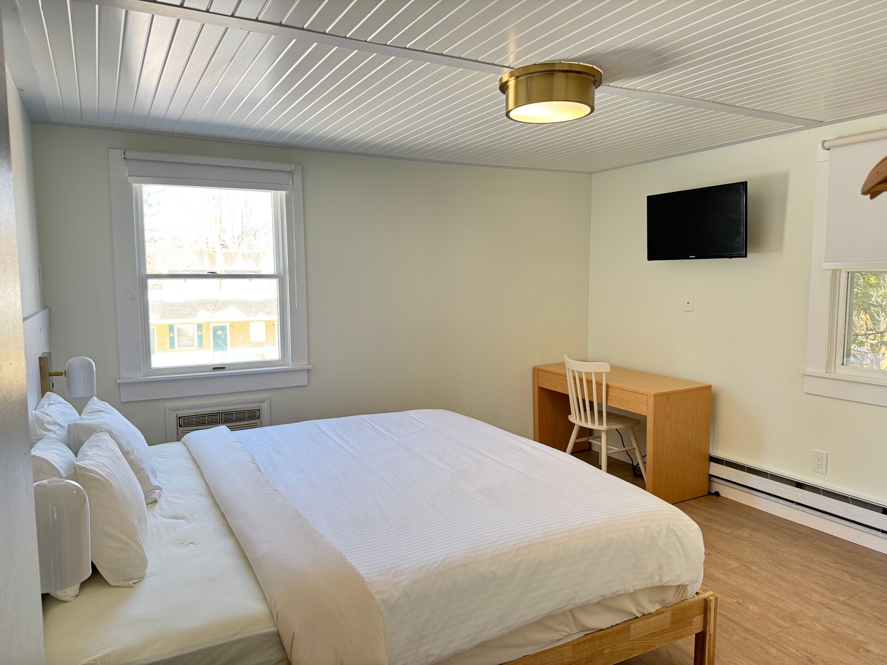 Un dormitorio con cama, escritorio, silla, televisor y ventana.