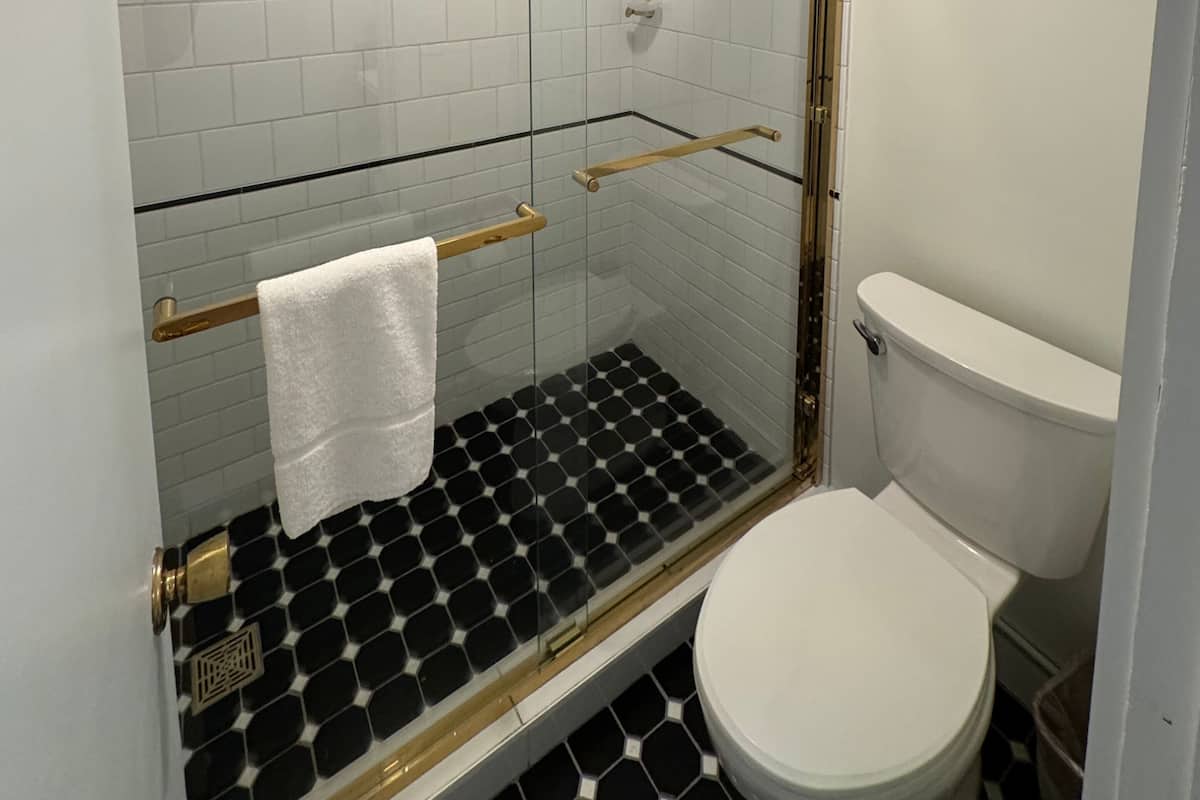 Um banheiro moderno com chuveiro em box de vidro, vaso sanitário branco e piso com ladrilhos preto e branco.
