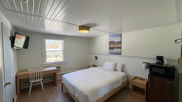 Et soveværelse med seng, skrivebord, stol, fjernsyn, vindue og mikroovn.