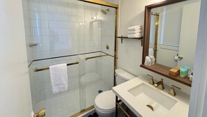 A modern bathroom with a glass-enclosed shower, white tiled walls, a white toilet, and a large mirror with a wooden frame. - Maple Leaf Inn - Lake Placid (Lake Placid)