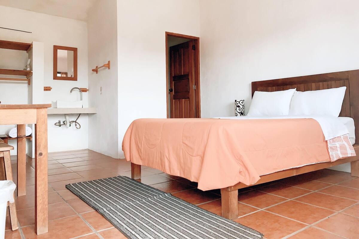 Un dormitorio con cama, cabecero de madera, mesita de noche, espejo y una puerta.
