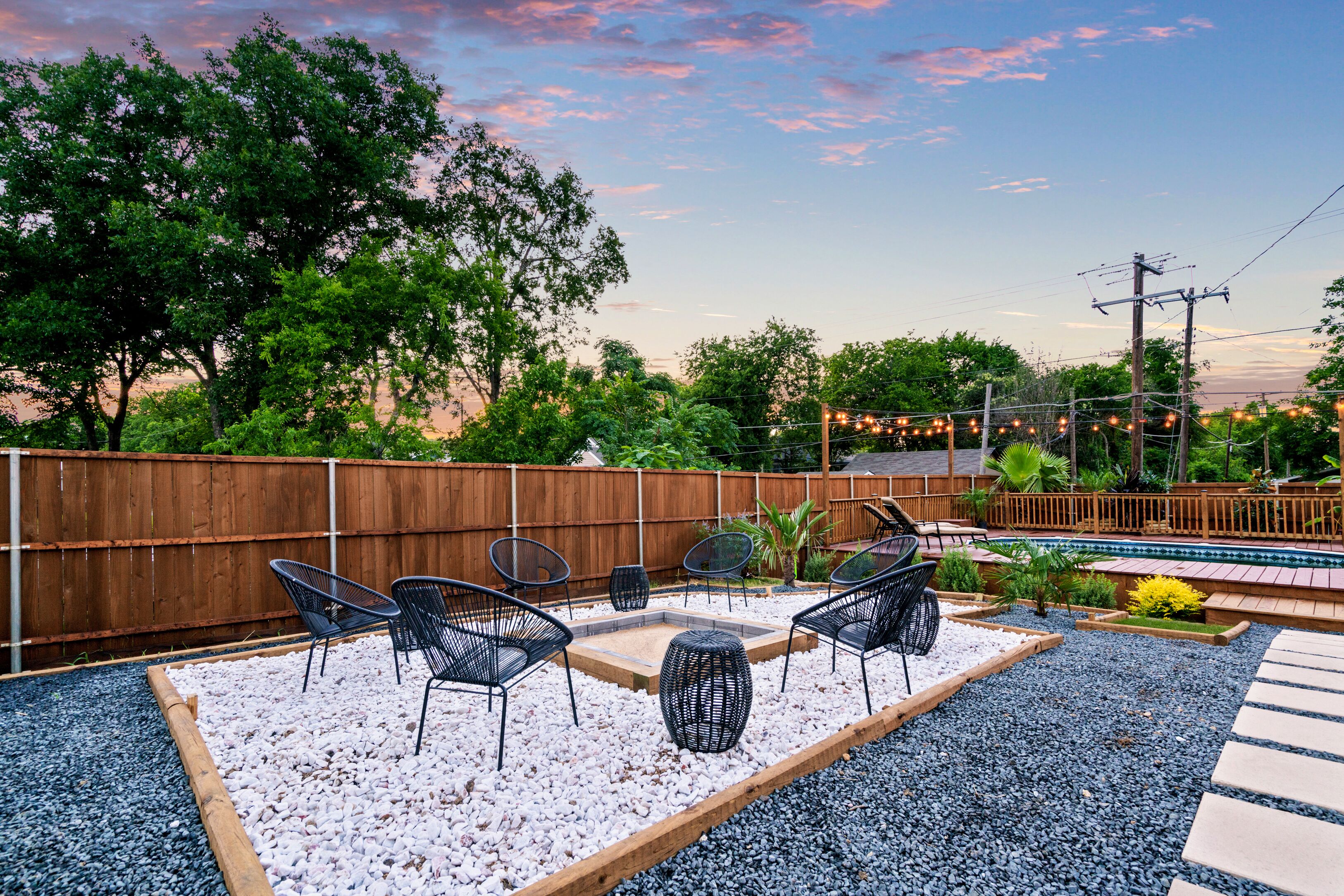 A backyard with a wooden fence, outdoor seating, a fire pit, and a pool.