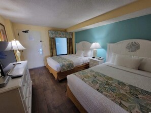 A hotel room with two beds, a desk with a computer, a lamp, and a window with curtains. - Monterey Bay by Escape (Myrtle Beach)