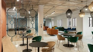 A modern interior with round tables and green chairs, a seating area with sofas, and hanging light fixtures. - The Archer Aparthotel by Totalstay (Sandton)
