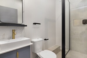 Casa de banho moderna com lavatório branco, torneira dourada e sanita.