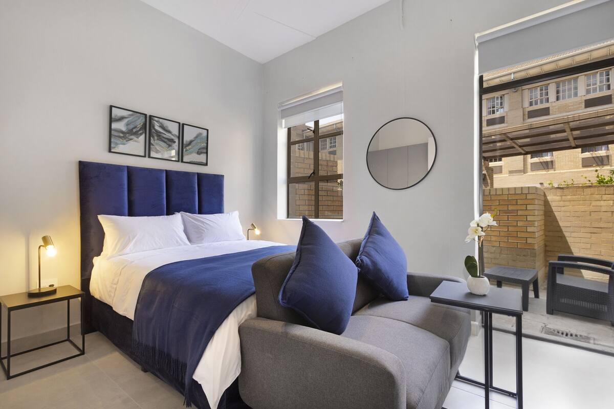 Un dormitorio moderno con cama, sofá, una mesita, espejo y obras de arte en la pared.