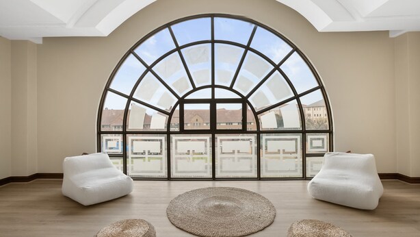 A spacious room with a large arched window, two white bean bag chairs, and a woven rug on a wooden floor. - The Archer Aparthotel by Totalstay (Sandton)