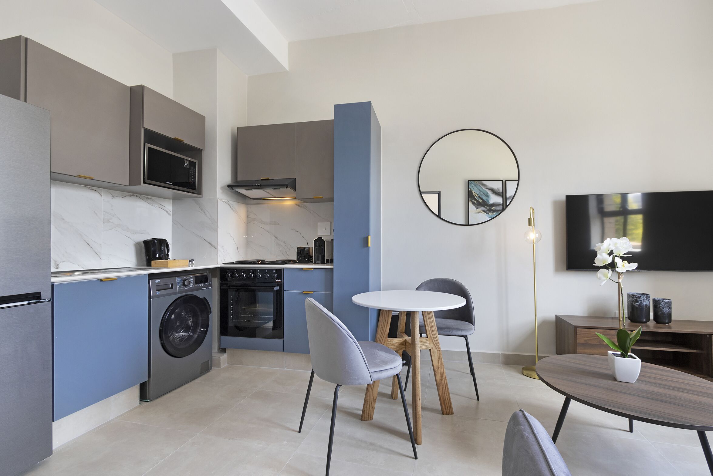 A modern kitchen with built-in appliances, a dining area with a round table and chairs, and a large mirror on the wall.