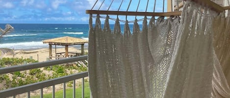 Eine Hängematte auf einem Balkon mit Blick auf einen Strand und klare Sicht aufs Meer.