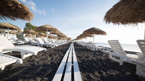 Una playa con hileras de sillas reclinables blancas y sombrillas de paja, que se extienden hasta el agua.