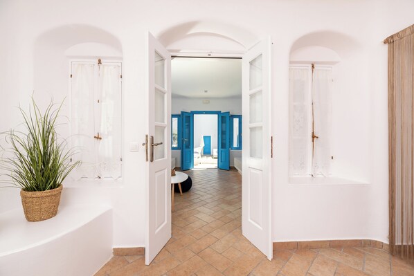 A hallway with white walls, a tiled floor, and a potted plant. - Seaside by Manos (Santorini)
