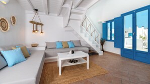 Una sala de estar moderna con un sofá blanco, cojines azules, una mesa de centro blanca y una escalera con puertas azules.