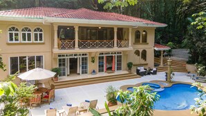 A two-story house with a swimming pool, outdoor furniture, and lush greenery. - Casa Bamboo with Guest House | Colonial Estate | Sleeps 14 | Manuel Antonio (Manuel Antonio)