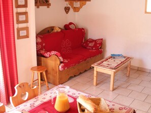 Een gezellige woonkamer met een houten bank, een klein houten tafeltje en een tafelkleed met een rood patroon.