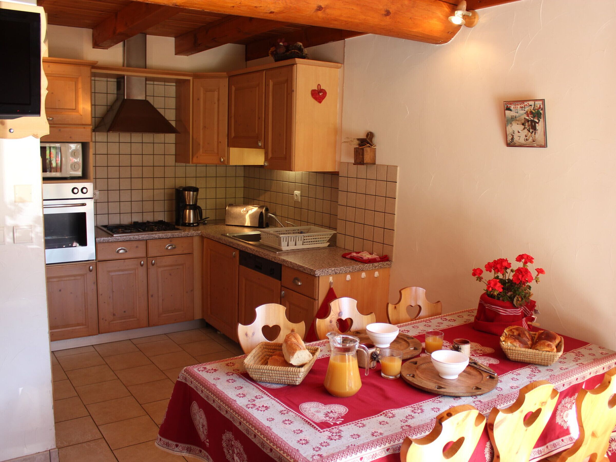 A kitchen with wooden cabinets, a tiled backsplash, a stove, and a dining table set with bread, a pitcher of juice, and bowls.