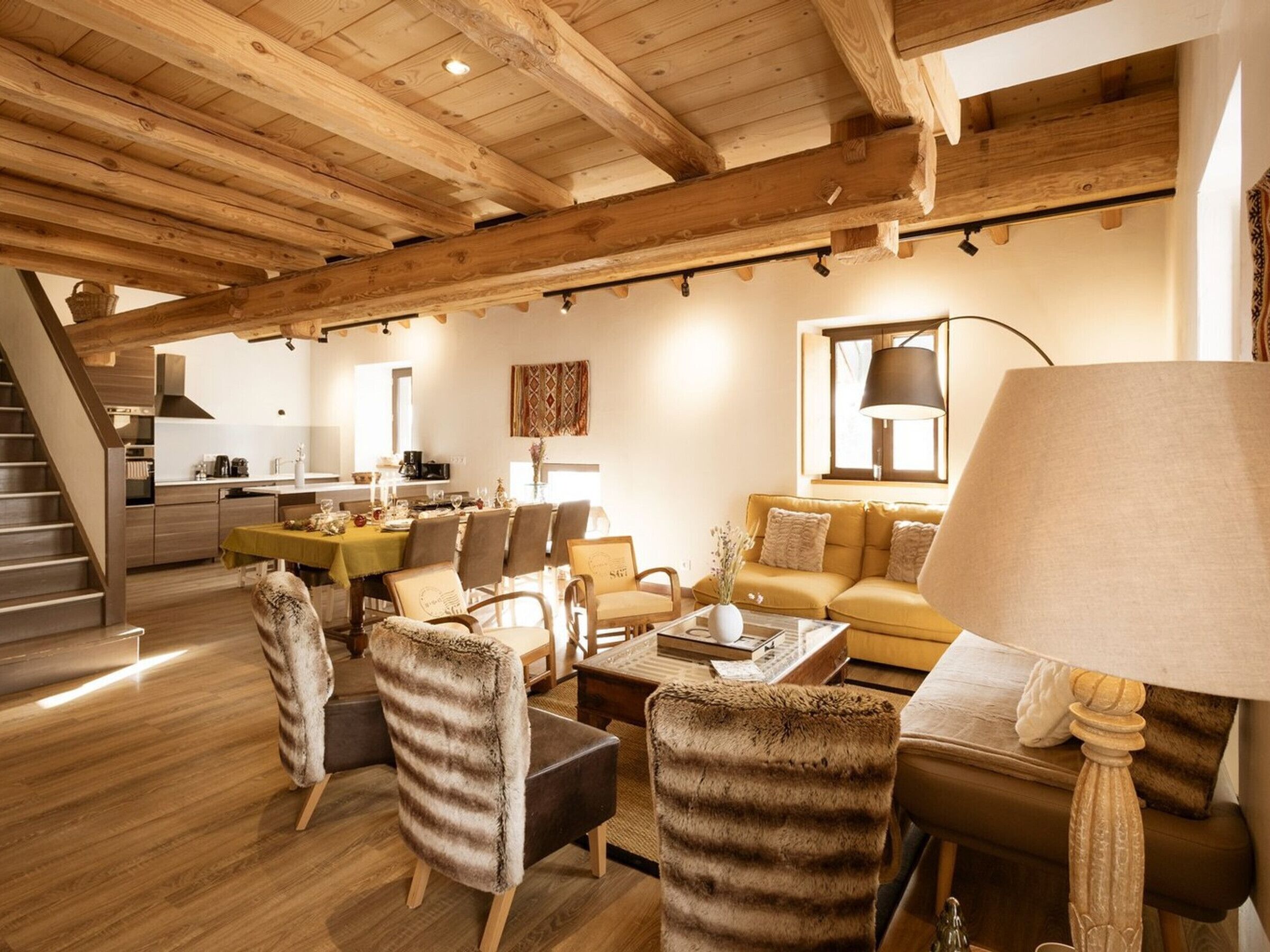 Amplia sala de estar con vigas de madera, un sofá, sillas y una mesa de comedor.