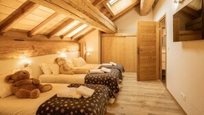 A cozy attic bedroom with wooden beams, a sloped ceiling, and skylights. There are two beds with floral bedding and a teddy bear on one bed. - Duplex 5 rooms for 10 people, pets allowed, balcony, parking (Valloire)