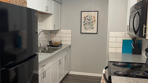 Una cocina moderna con armarios blancos, un refrigerador negro, una estufa y un microondas.